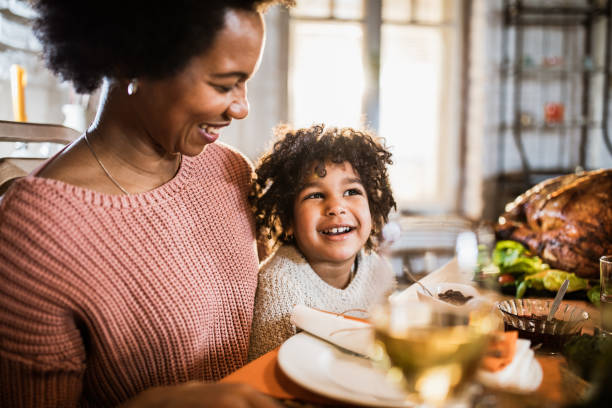 Happy black single mother and her daughter on Thanksgiving meal at dining table.