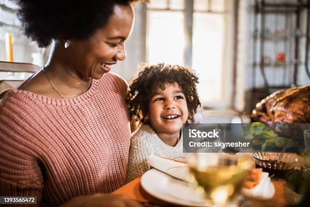 Happy black single mother and her daughter on Thanksgiving meal at dining table.