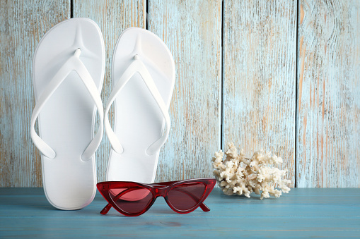 Stylish flip flops, coral and sunglasses near wooden wall