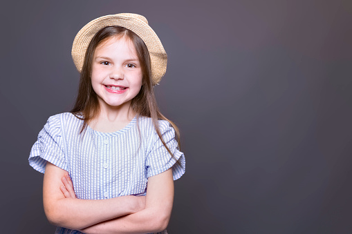 Black and white portrait of a 12-year-old girl. It's summer. She wears a light top and cap. She holds a blade of grass between her lips. She smiles and looks at the photographer. She is happy and sports small dimples.