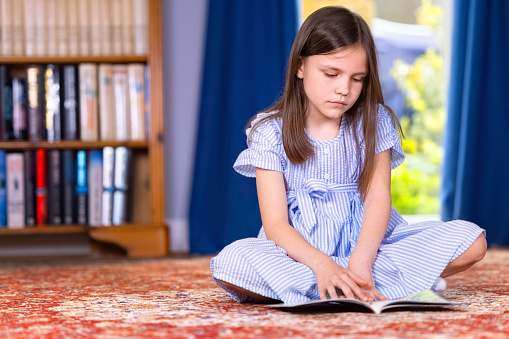 Brown-haired girl of seven wearing a striped dress and reading a book.