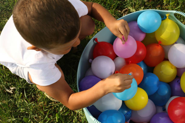 緑の芝生に水爆弾の洗面器を持つ小さな男の子、トップビュー - child balloon outdoors little boys ストックフォトと画像