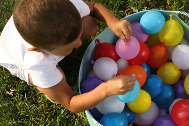 маленький мальчик с тазом водяных бомб на зеленой траве, вид сверху - child balloon outdoors little boys стоковые фото и изображения