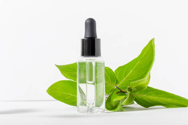 istock Transparent glass bottle with a dropper with moisturizer on a white background. Natural cosmetic face serum with hyaluronic acid with green leaves 1393569010