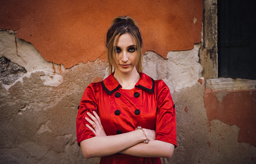 Portrait of a young confident woman in a red dress in Venice. She has her arms crossed and looks directly at the viewer.