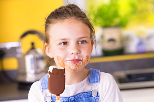Brown-eyed 7 year old girl eating a chocolate ice cream lollipop.