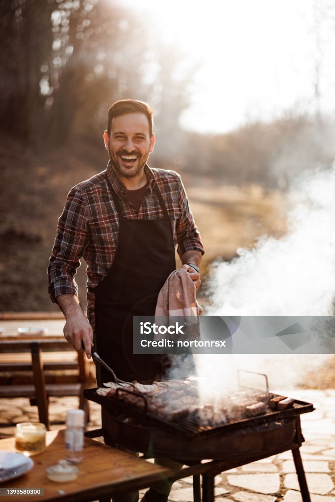 Portrait of a smiling man, making a lunch outside, preparing bar Smiling man with an apron, holding a cloth and accessories for the barbecue. Barbecue - Meal Stock Photo