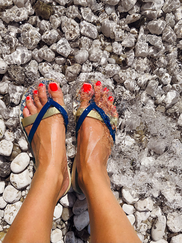 Female feet with red nail polish standing in shallow water