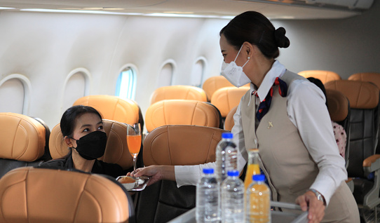 Air hostess  wearing protective face mask service  for passengers on the airplane ,Cabin crew pushing service cart and serve to customer on the airplane during flight. New normal, flight attendant