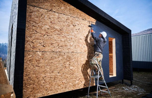 istock Male painter using paint roller, doing exterior paint work while building wooden frame house. 1393583999