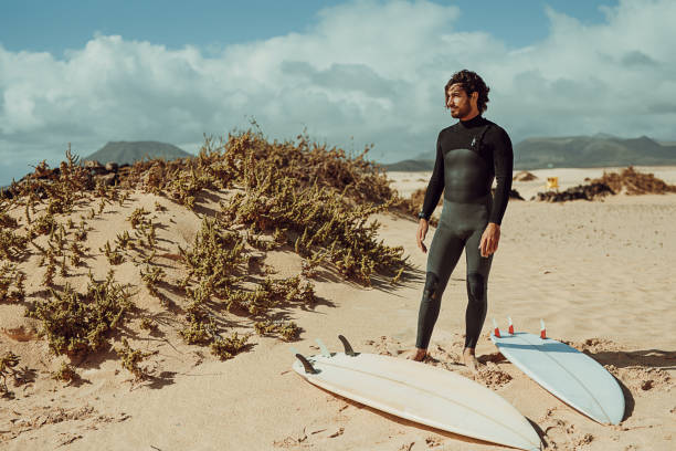 istock Handsome surfer in the wetsuit standing on the beach 1393584044