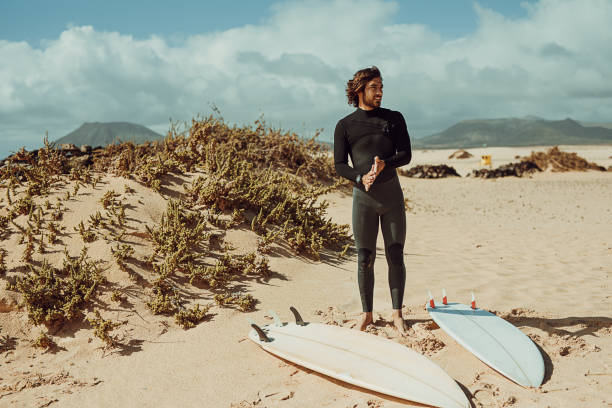 istock Handsome surfer in the wetsuit standing on the beach 1393584074