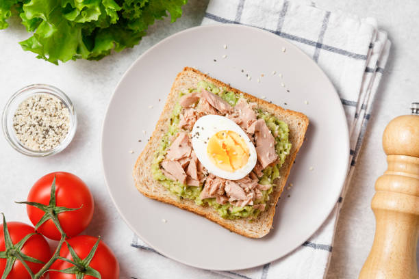 istock Avocado rye bread toast with tuna and boiled egg on bright background. Healthy appetizer, breakfast, lunch or snack. Top view, close up 1393584328