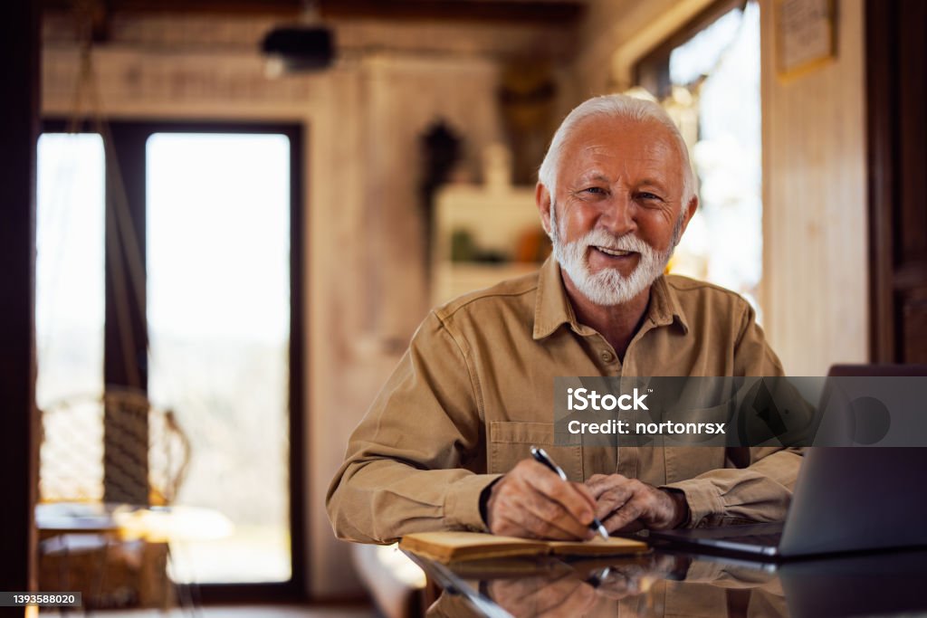Portrait of a smiling senior man, looking at the camera while wr Portrait of a bearded mature man, posing for the camera, holding a pen. 65-69 Years Stock Photo