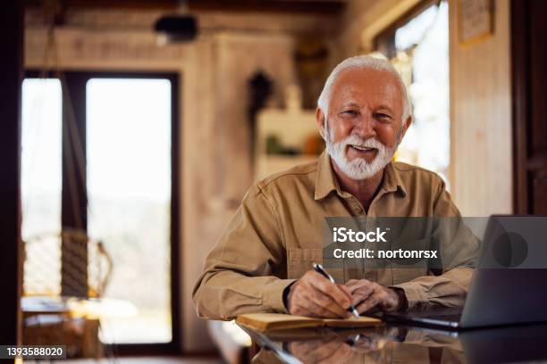 Portrait Of A Smiling Senior Man Looking At The Camera While Wr Stock Photo - Download Image Now