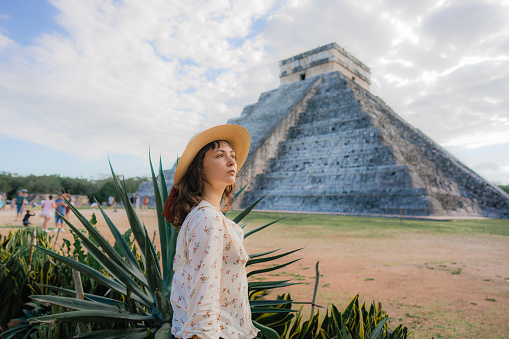 Side view of  young Caucasian  woman in hat  standing  on the background of Chichen Itza pyramid in Mexico
