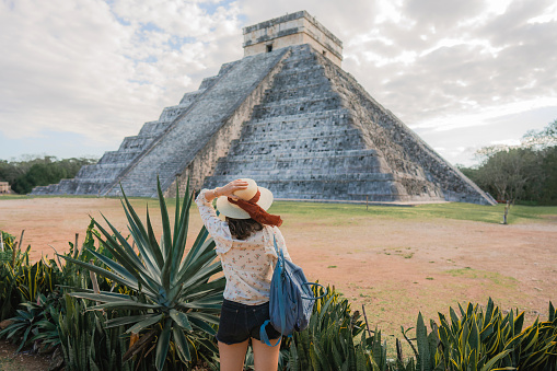 Rear view of young Caucasian  woman in hat  standing  on the background of Chichen Itza pyramid in Mexico
