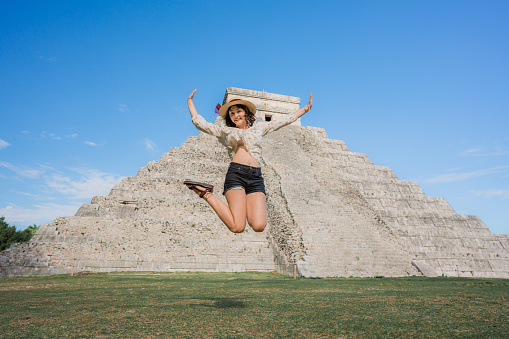 Young Caucasian woman  jumping near Chichen Itza pyramid in Mexico