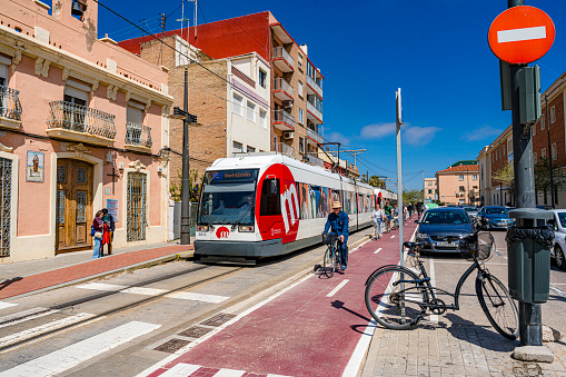 Valencia-Spain April 23, 2022. Metro train and tourists riding bicycles on bicycle lane at La Malvarrosa