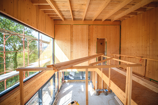 Interior of a wooden construction frame with big windows on the left. Plenty of natural light comes through the windows.