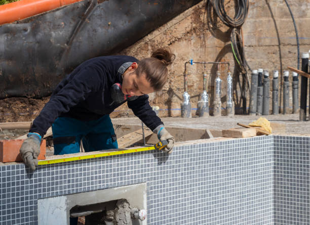 Young working man taking measurements in a swimming pool under construction in the middle of a construction site