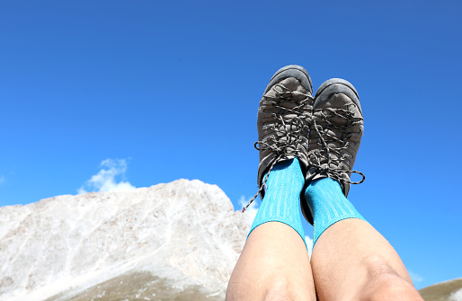 two hiking boots of the hiker while resting with high legs and the mountain in the background