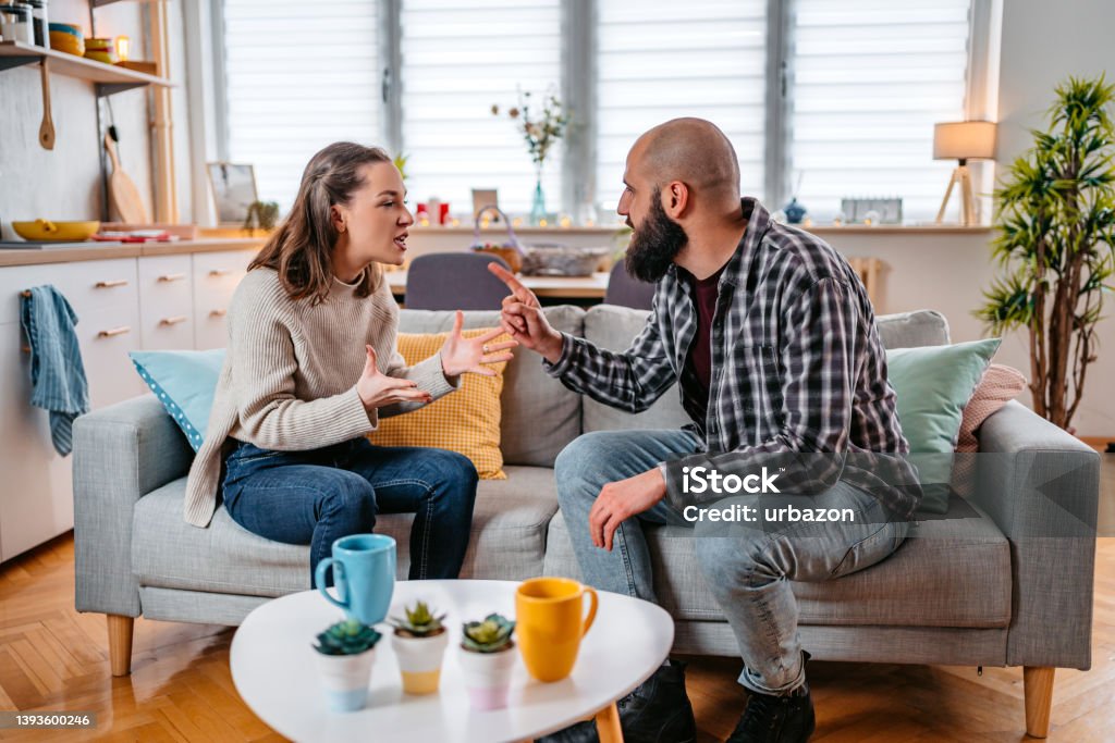 Young Couple Arguing At Home Young couple with relationship problems arguing on the sofa in the living room. Arguing Stock Photo