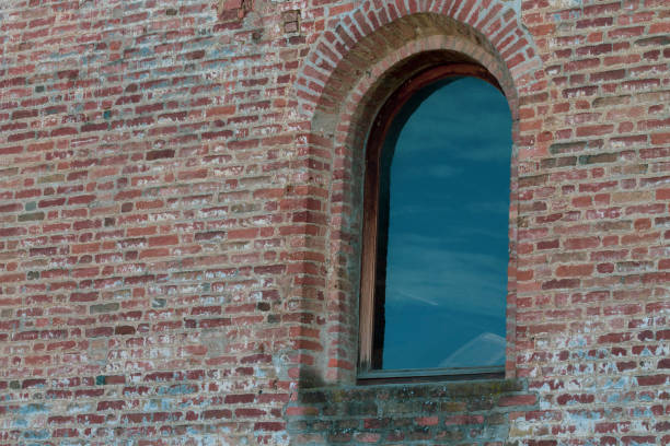 istock Low angle view of an old stone window reflecting sky and clouds. 1393600355