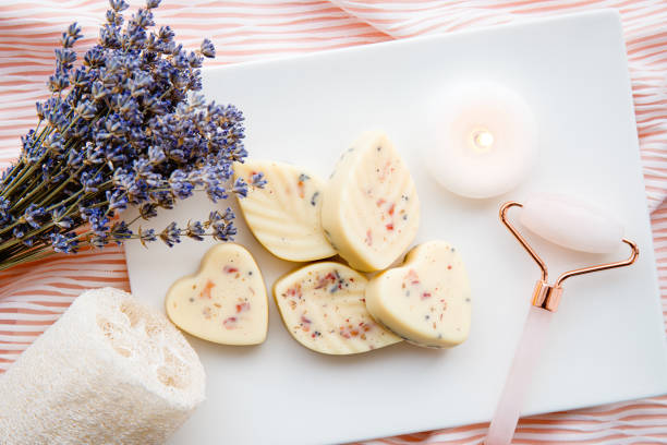 truffes de bain en forme de petit cœur et de feuille, version beurrée de la bombe de bain dans la salle de bain sur plateau blanc avec bougie allumée et outil de roulement du visage en quartz rose. concept de spa à domicile. - fondant parfumée photos et images de collection