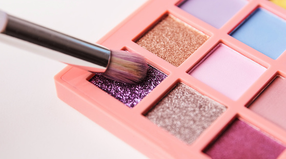 Make up artist picks purple shimmer pigment from bright colorful eyeshadow palette with a brush. Decorative cosmetics and visage concept. Selective focus.