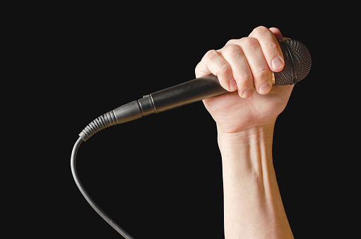 Microphone in hand closeup. Isolated on a black background.