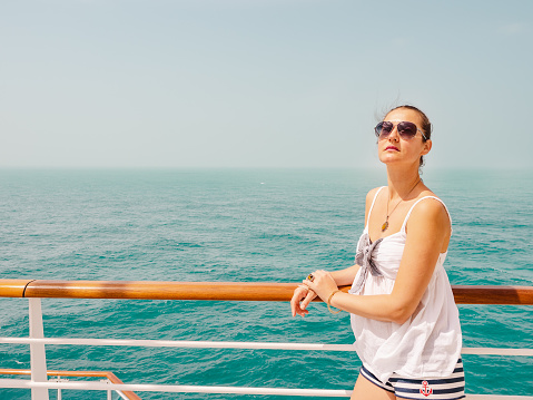 Beautiful woman standing on the empty deck of a cruise liner. Closeup, outdoor. Vacation and travel concept