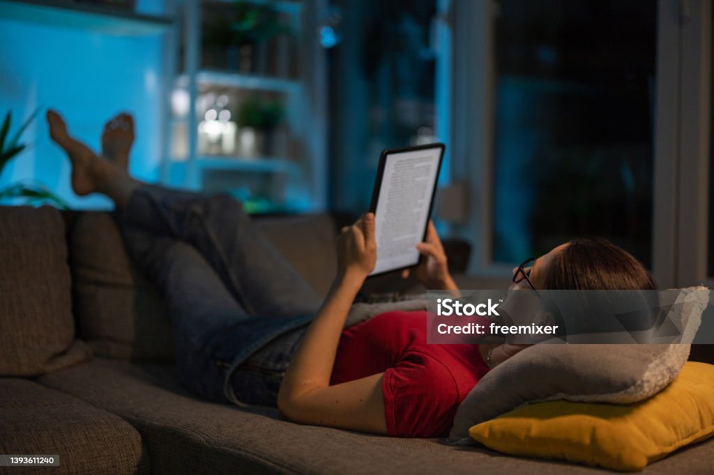 Reading digital book Woman lying on sofa in living room at home, and reading a book on digital tablet in peace. E-Reader Stock Photo
