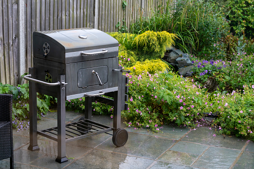 A charcoal barbecue rusting in the rain in an English country garden.