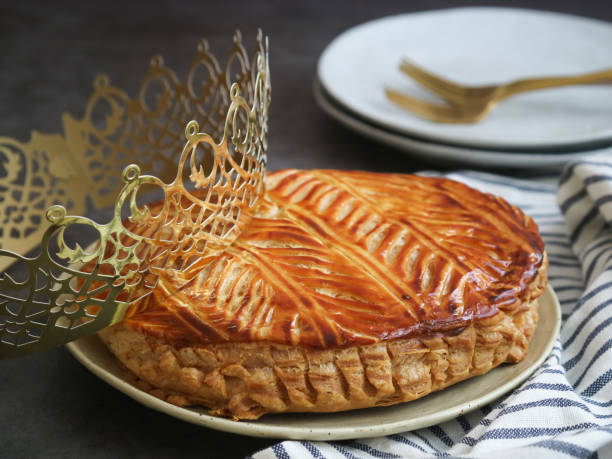 A traditional French galette des rois on a plate A traditional French galette des rois on a plate with crown, plate and cutlery in background. Cake made with puff pastry and creamy almond filling roll in circle shape. It's usually served on Epiphany galette stock pictures, royalty-free photos & images