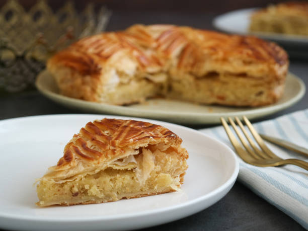 A cut piece of traditional French galette des rois or King cake with crown A cut piece of traditional French galette des rois or King cake with crown, it's a cake made with puff pastry and creamy almond filling roll in a circles shape. It's a cake associated with Epiphany galette stock pictures, royalty-free photos & images