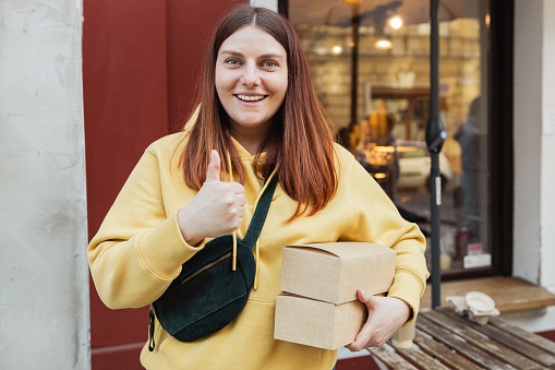 Happy smiling Woman Hands holding two take-out food containers near restaurant. Fast food eco packaging with big breakfast set. Recycle environment friendly.