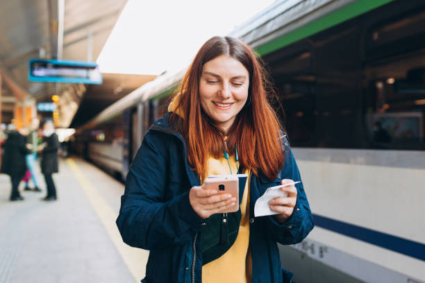 istock Young redhhead woman waiting on station platform with backpack on background electric train using smart phone. Railroad transport concept, Traveler 1393614396