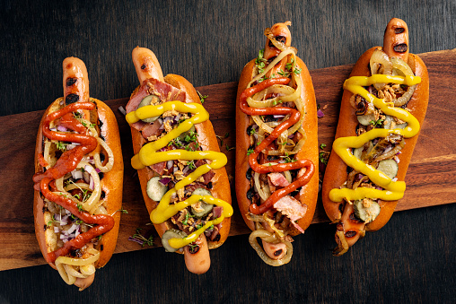 Overhead view of four artisan hot-dogs in brioche rolls with pickles and relishes. Colour, horizontal format with  some copy space.