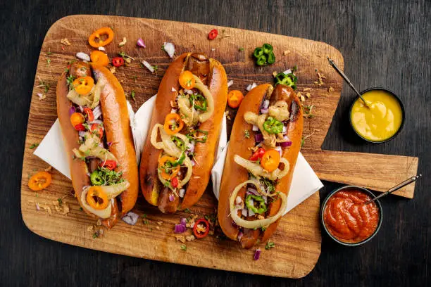 Overhead view of three artisan hot-dogs in brioche rolls with pickles and relishes. Colour, horizontal format with  some copy space.