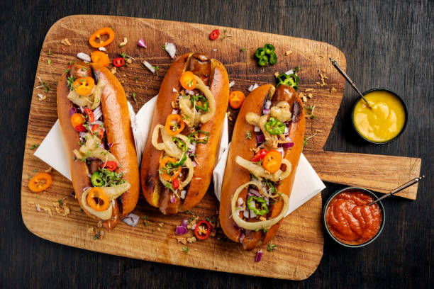 artisan hot dogs in brioche rolls with pickles, onion and relishes. - hot dog imagens e fotografias de stock