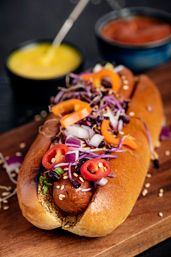 Close-up, shallow focus view of a vegetarian hot-dog in brioche roll with pickles and relishes. Colour, vertical format with some copy space.