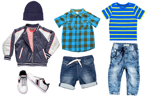 Collage set of little boys spring clothes isolated on a white background. Denim trousers or pants, short jeans, sneaker, a rain jacket, shirts and a cap for child boy. Children's summer fashion.