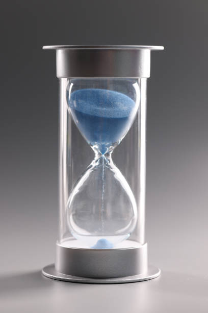 istock Hourglass with blue sand on gray background 1393619548