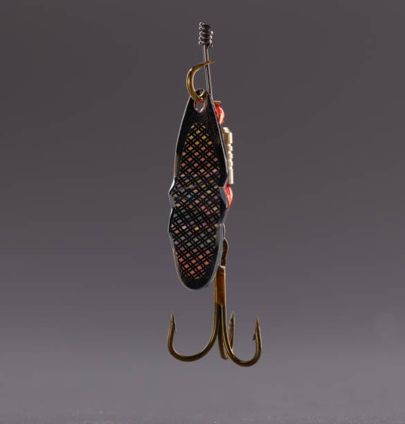 Close-up of fishing hook, sharp tip of hook or construction to catch fish in river or lake, hunting and fishing. Fishing lure wobbler on grey background