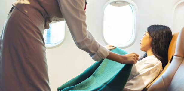 happy stewardess looking after an adult businesswoman passenger, air hostess or flight attendant woman covering tired sleeping passengers with blanket throughout journey - color image people air vehicle airplane imagens e fotografias de stock