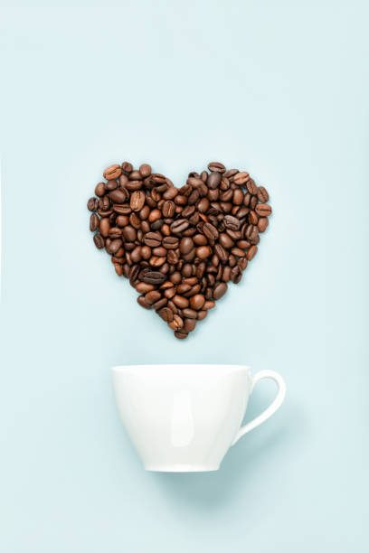 White coffee cup and coffee beans in shape of heart on blue background, flat lay stock photo