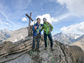 Two Mountaineers men stand on a mountain top below the summit cross