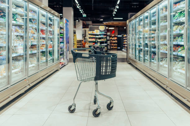 Supermarket aisle with empty black shopping cart Empty shopping cart in the aisle of the supermarket in front of freezers frozen food stock pictures, royalty-free photos & images
