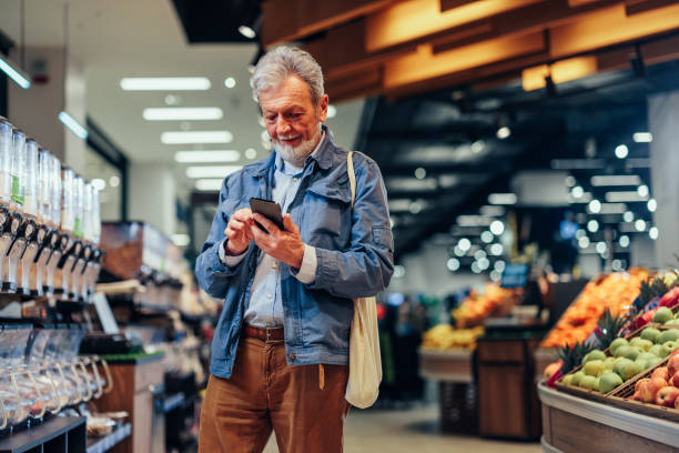 istock Mature man using phone while shopping in supermarket 1393629892